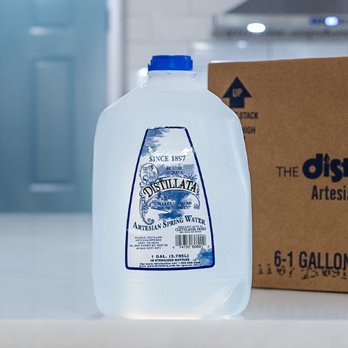 1 gallon bottle of Distillata spring water on a kitchen counter with a cardboard case in the background