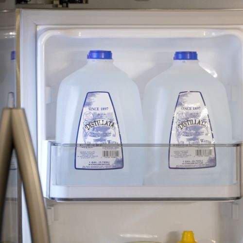 two 1-gallon bottles of Distillata spring water on refrigerator shelf