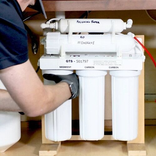 Person changing filters on an under-sink reverse osmosis water filtration system.