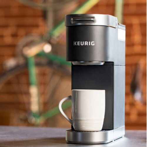 black keurig mini coffee brewer sitting on gray counter with red brick wall in background
