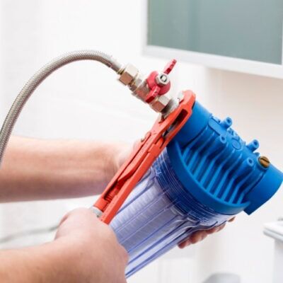 A plumber installing a water filter under a sink.