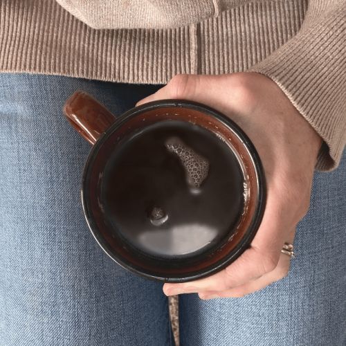 Hand holding brown mug filled with coffee in lap
