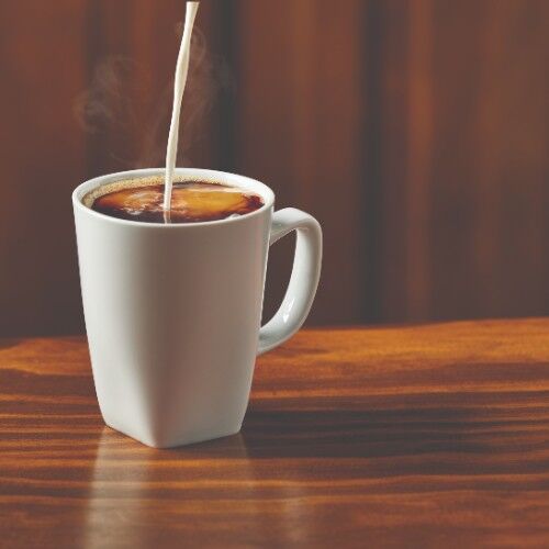 pouring cream into a mug of coffee sitting on a wood table
