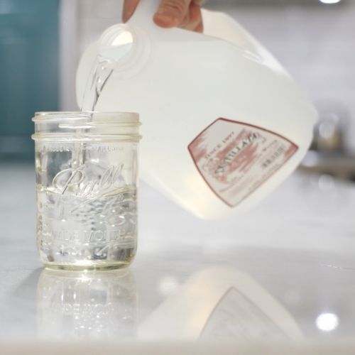 pouring Distillata 1 gallon distilled water into a mason jar glass in kitchen setting