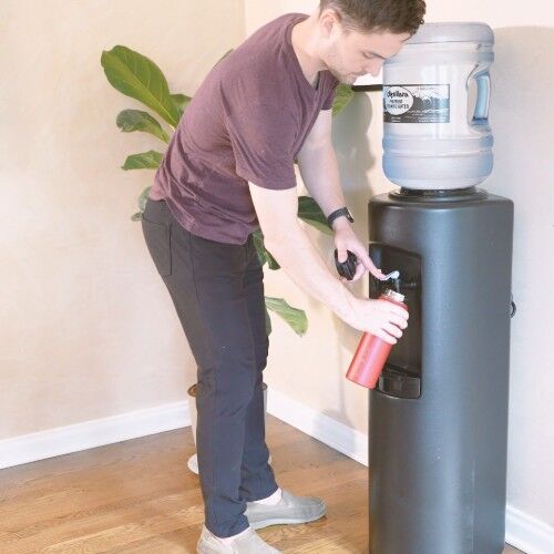 filling a red reusable water bottle from a black water dispenser with a 5-gallon water bottle on top